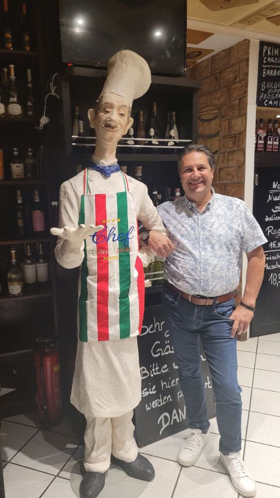 Pino lacht neben der Kochfigur am Eingang des Firenze
